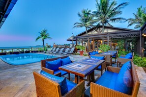 A poolside area with wicker furniture and a view of the ocean.