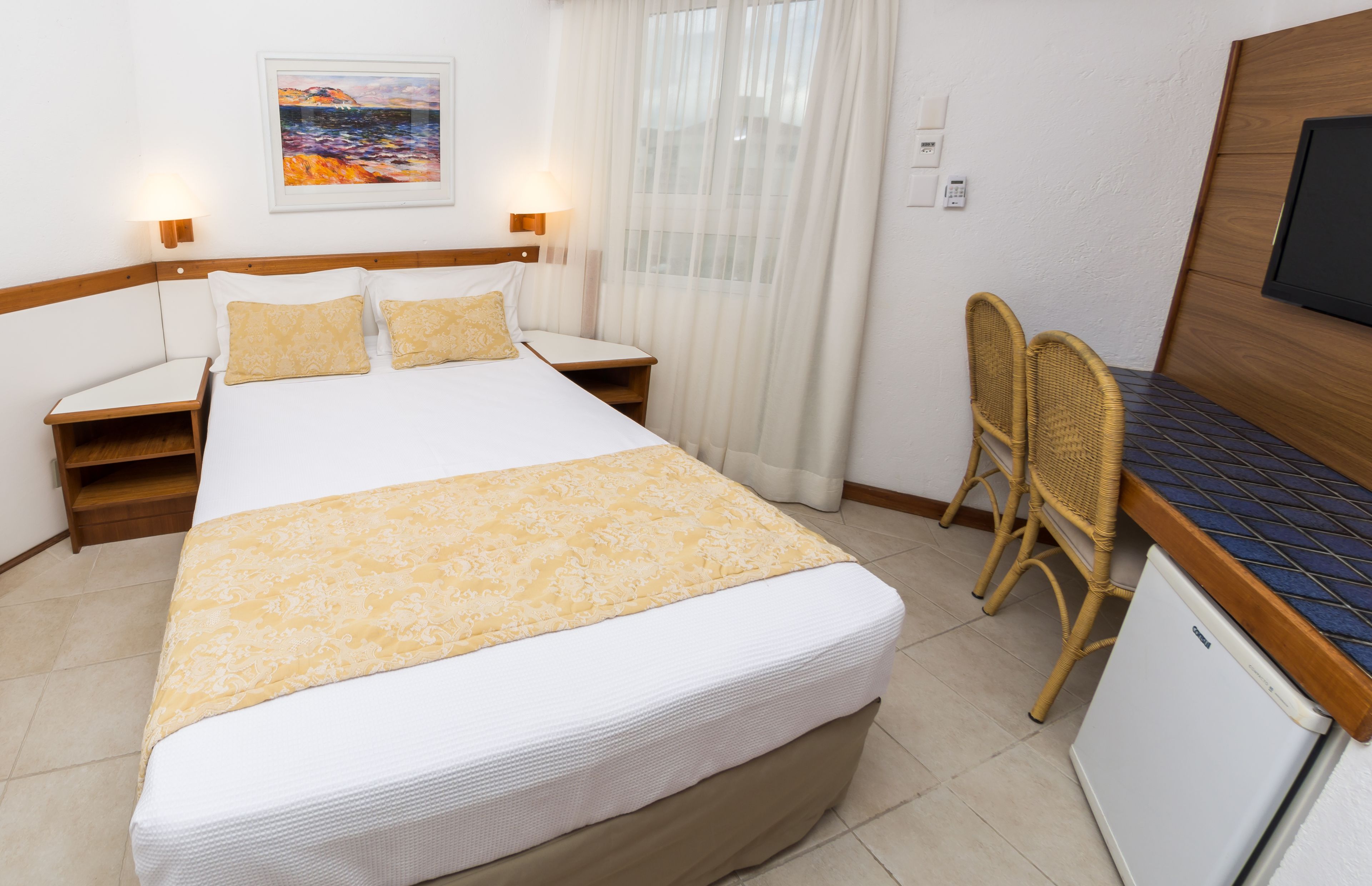 A hotel room with a bed, bedside tables, a desk with a chair, a television, and a painting on the wall.