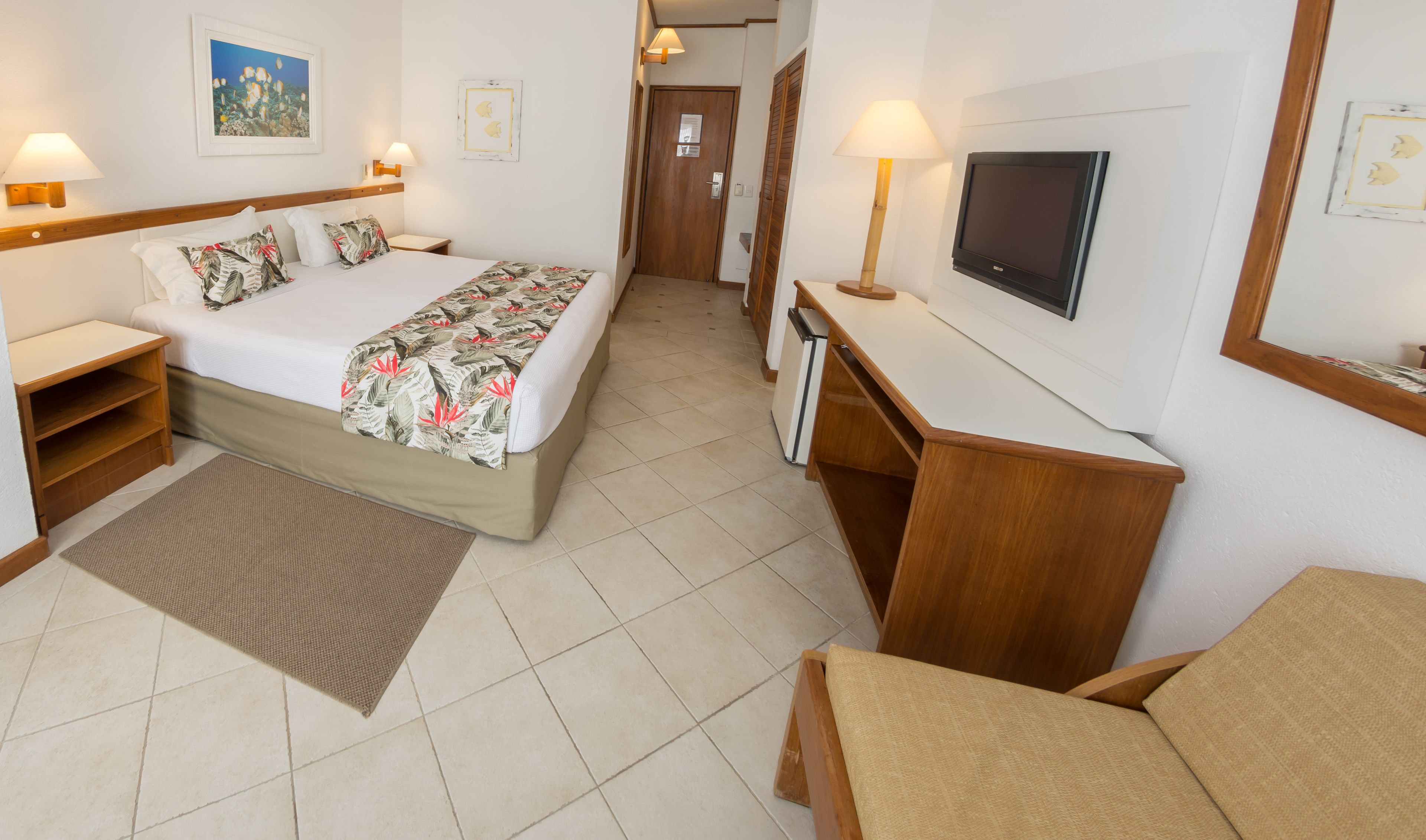 Habitación de hotel con cama, mesitas de noche, escritorio, televisor y puerta que da a otra habitación.