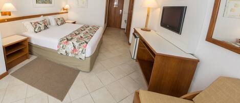 A hotel room with a bed, bedside tables, a desk, a television, and a door leading to another room.