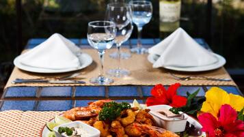 Mesa com frutos do mar, copos e uma garrafa, com vista para a praia.