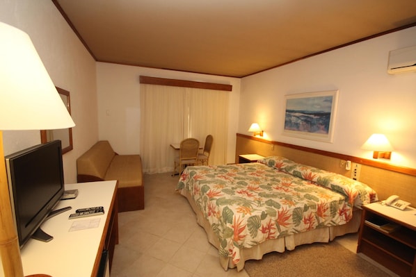 A hotel room with a bed, a desk with a TV, a chair, a desk lamp, and a painting on the wall. - Costa Norte Ingleses (Florianópolis)