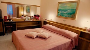A hotel room with a large bed, a desk, a chair, a mirror, and a painting on the wall. - Europa (Modena)