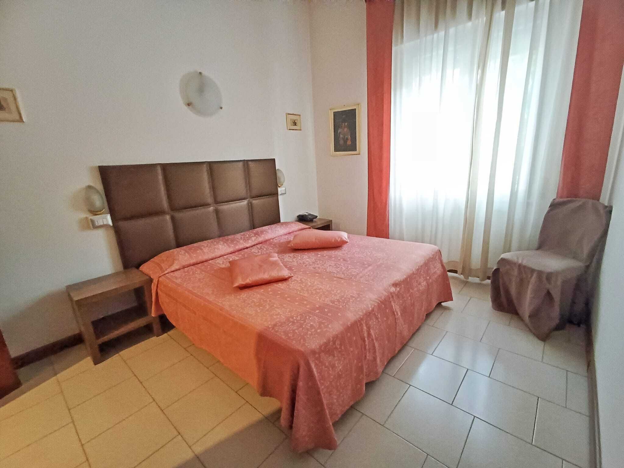 Una habitación de hotel con cama, mesita de noche, silla y ventana con cortinas.