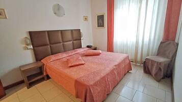 Una habitación de hotel con cama, mesita de noche, silla y ventana con cortinas.