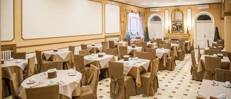 A banquet hall with round tables, chairs, and a stage with a large mirror and two lamps.