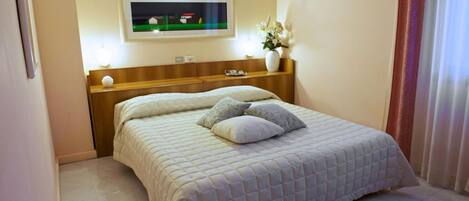 A hotel room with a bed, a nightstand, a vase with flowers, and a wall-mounted TV.