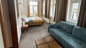 A room with a sofa, a bed, and a small table. There are windows with curtains, and a door is visible. - Hotel Radnice (Liberec)