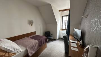 Una habitación de hotel pequeña y moderna con una cama, un escritorio, una silla, un televisor y una ventana.
