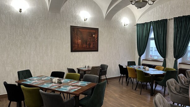A dining area with wooden tables, green and black chairs, and a large painting on the wall. - Hotel Radnice (Liberec)