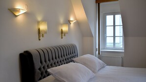 A bedroom with a tufted headboard, a large window, and wall-mounted lighting fixtures. - Hotel Radnice (Liberec)
