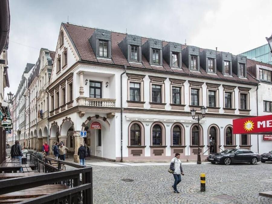 A cobblestone street with historic buildings, a Merkur gas station, and outdoor seating.