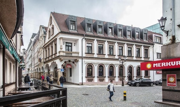 A cobblestone street with historic buildings, a Merkur gas station, and outdoor seating.