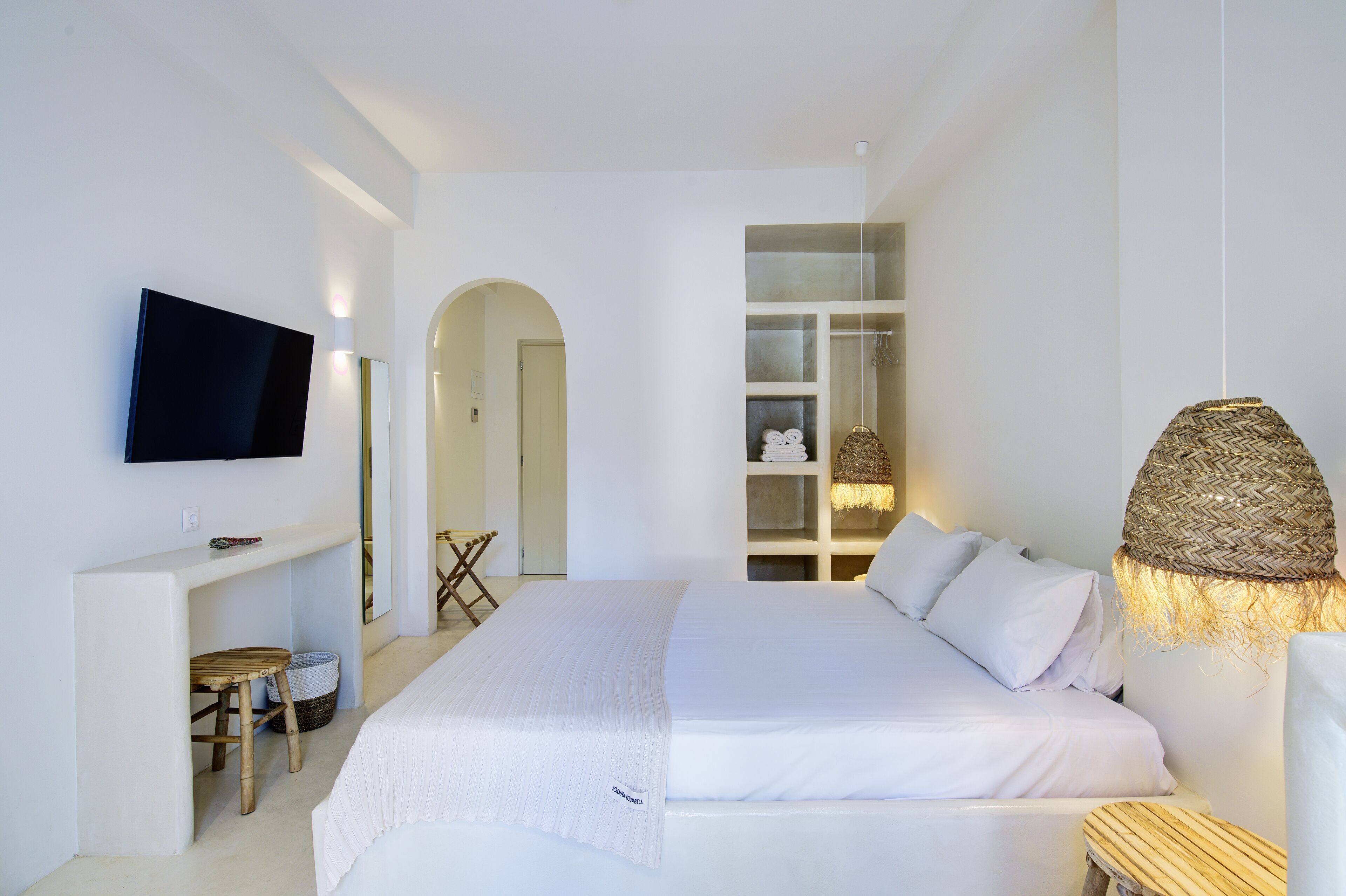 Un dormitorio moderno con cama, televisor montado en la pared, escritorio con silla y estantería.