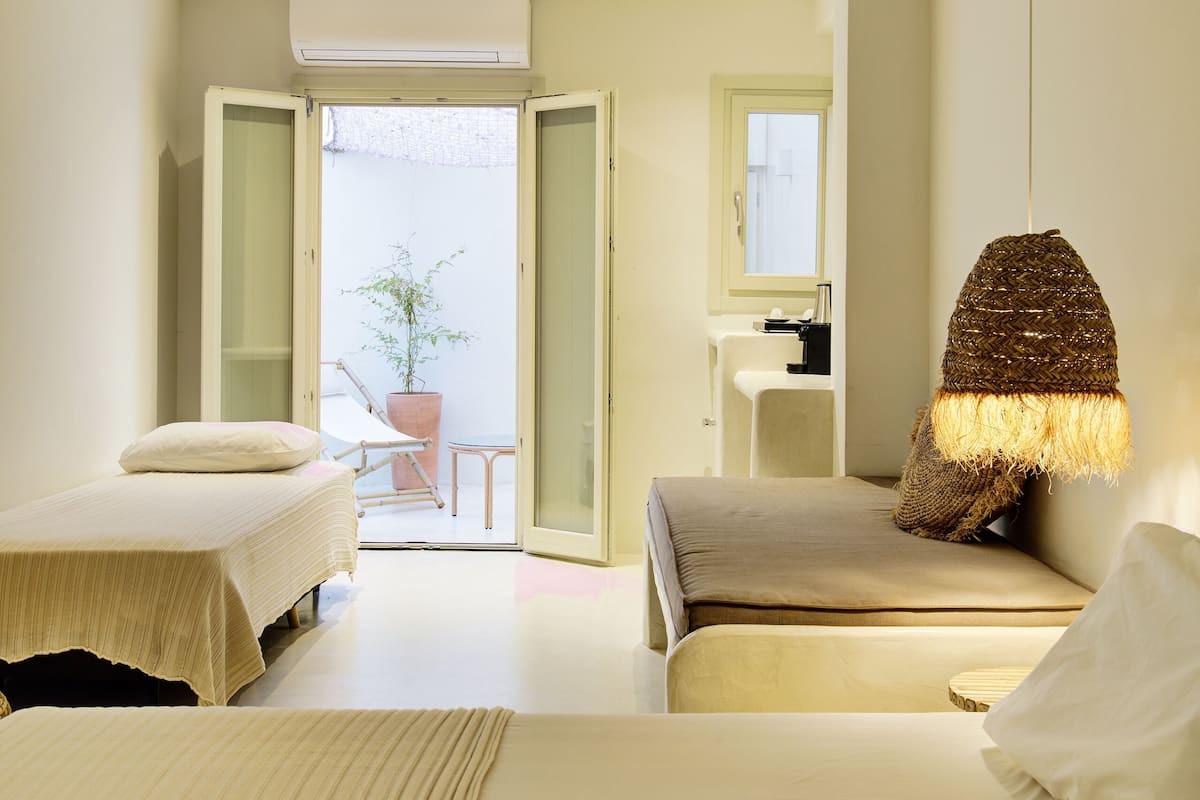 Ein Hotelzimmer mit zwei Betten, einer Hängelampe, einer Topfpflanze und Blick ins Freie.