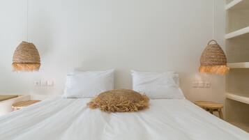 Un lit avec une literie blanche, deux oreillers blancs et un plaid tissé. Deux lampes suspendues tissées sont accrochées au-dessus du lit.