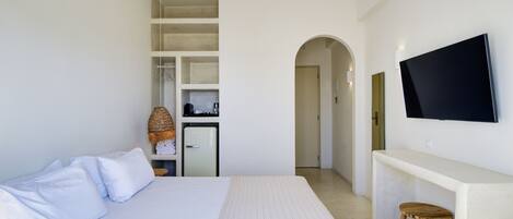 A hotel room with a large bed, a TV mounted on the wall, a small kitchenette, and a wooden stool.