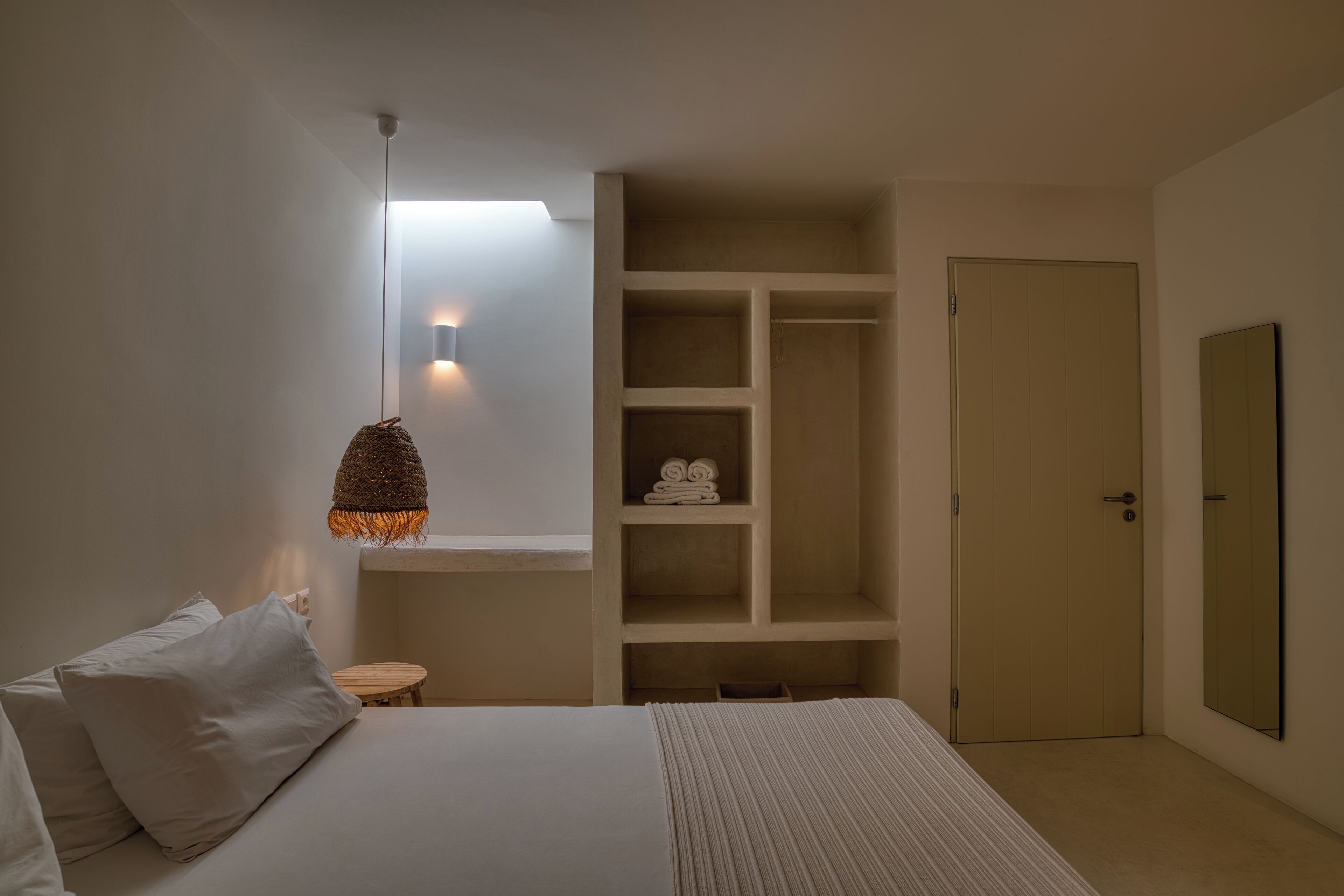 A bedroom with a bed, a bedside table, a hanging light fixture, a wardrobe, and a door.