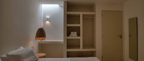 A bedroom with a bed, a bedside table, a hanging light fixture, a wardrobe, and a door.