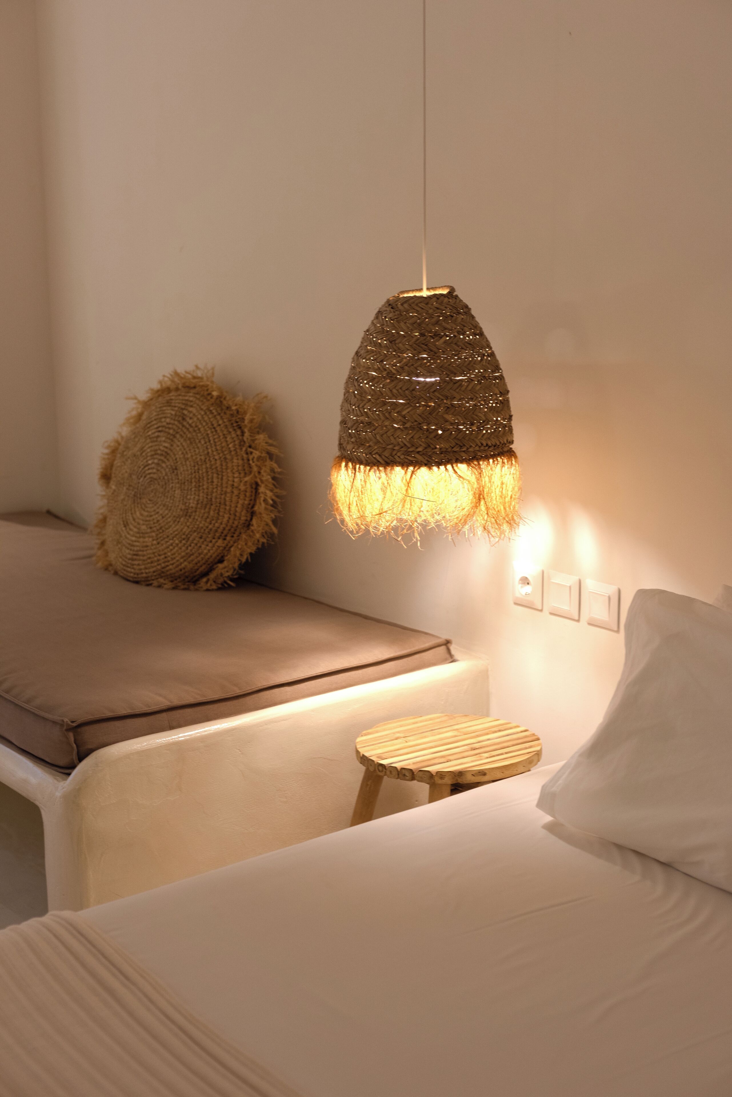 A bedroom with a bed, a small wooden stool, a textured hanging light fixture, and a wall-mounted switch.