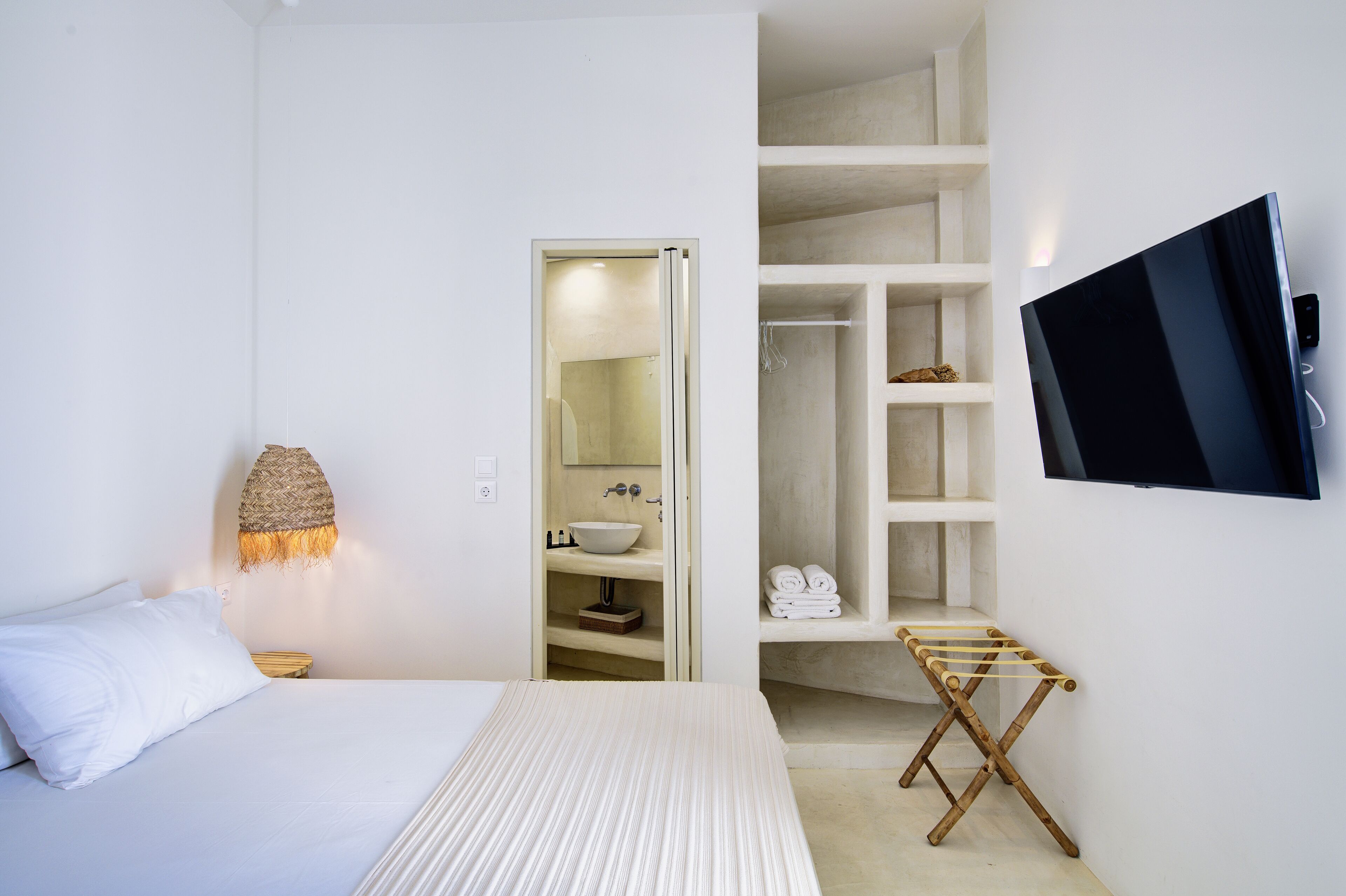 Un dormitorio con cama, lámpara de noche, televisor montado en la pared y vestidor con estantes y espacio para colgar ropa.