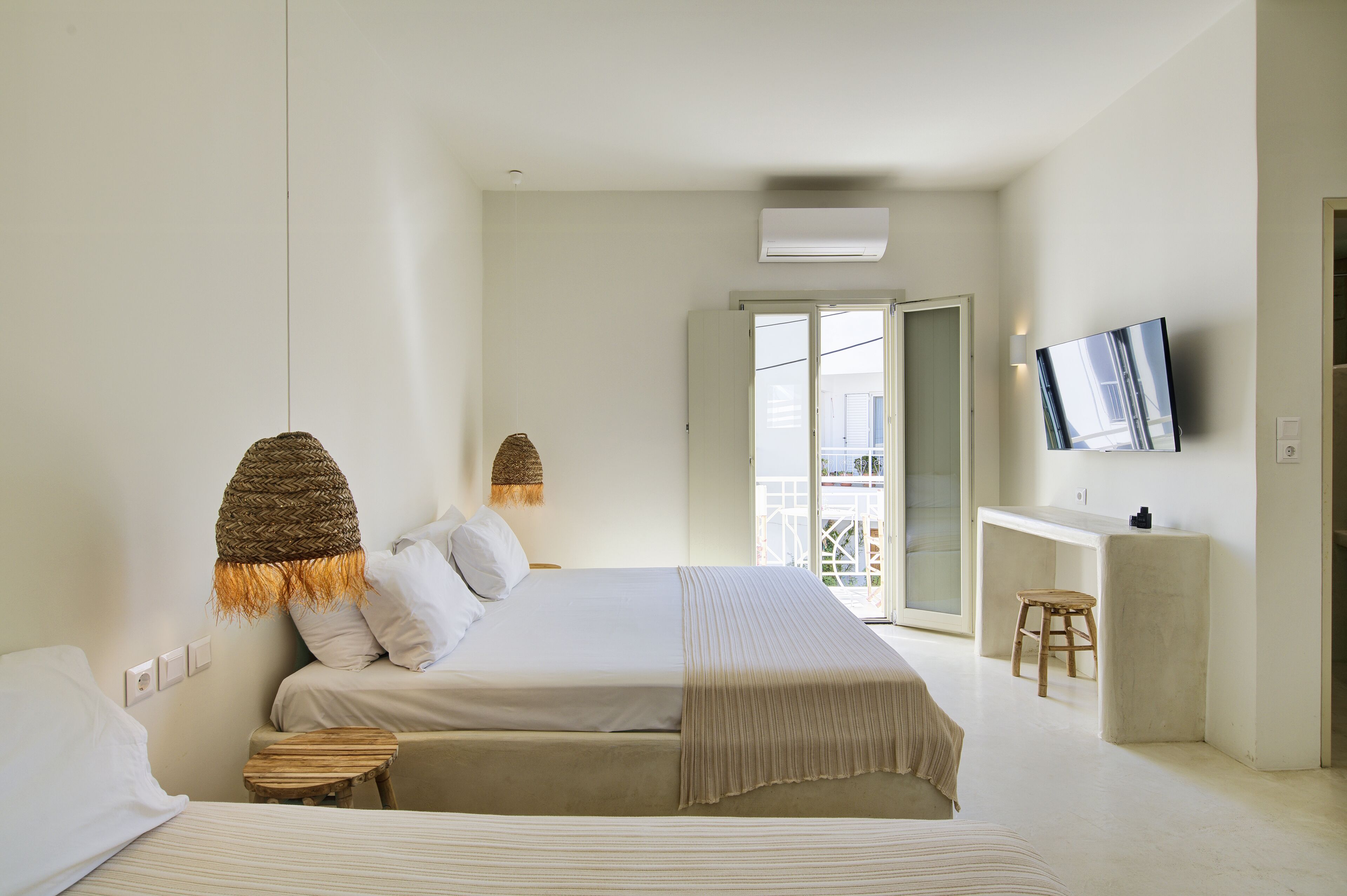A modern bedroom with a large bed, bedside tables, a small stool, and a TV mounted on the wall.