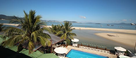 Un área de piscina con vistas a la playa y el océano, rodeada de palmeras y sillas de playa.