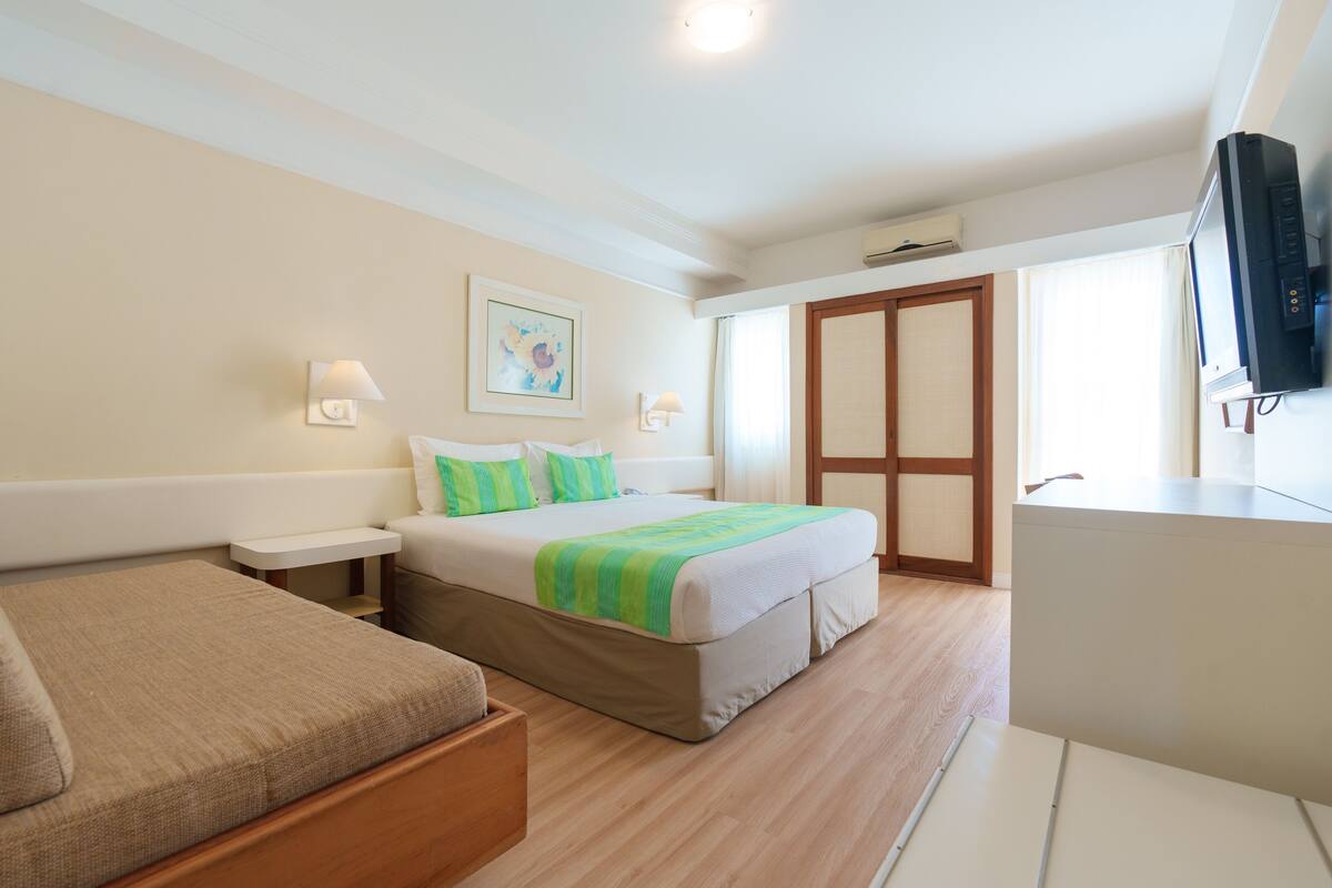 A hotel room with a bed, a sofa, a TV, and a window.