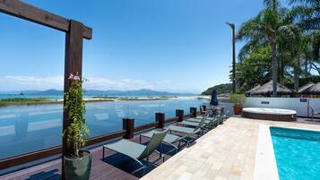 An infinity pool with a view of the ocean and mountains, lounge chairs, and a hot tub.