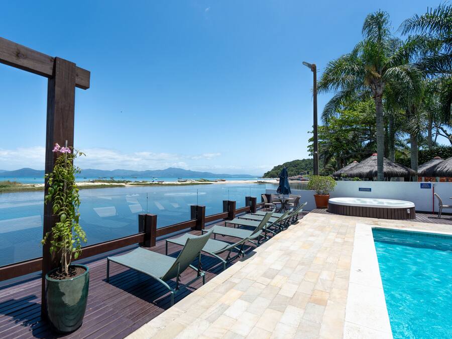 An infinity pool with a view of the ocean and mountains, lounge chairs, and a hot tub.
