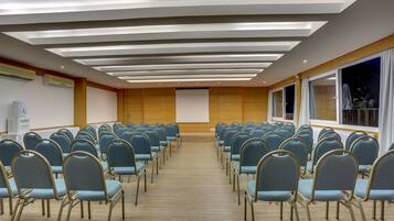 Un salón de conferencias con filas de sillas, una pantalla de proyector y un ventanal grande.