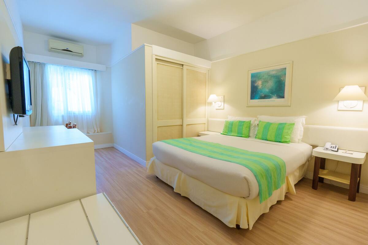 A hotel room with a bed, bedside table, lamp, and a painting on the wall.