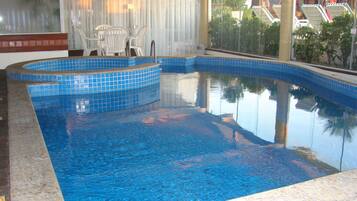 Una piscina con azulejos azules, una zona de estar con sillas y vistas a palmeras y un edificio.
