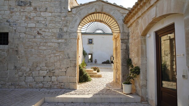 A stone building with a cobblestone pathway leading to an arched entrance. - Torre Dantona (Modica)