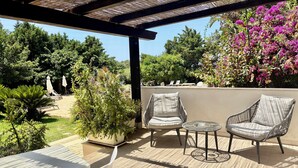 An outdoor seating area with wicker chairs and a round table, surrounded by lush greenery and flowering plants. - Torre Dantona (Modica)