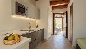 A narrow kitchen with a built-in microwave, a sink, and a wooden ceiling. A wicker basket with lemons is on the counter, and a bottle of wine is on the sink. - Torre Dantona (Modica)