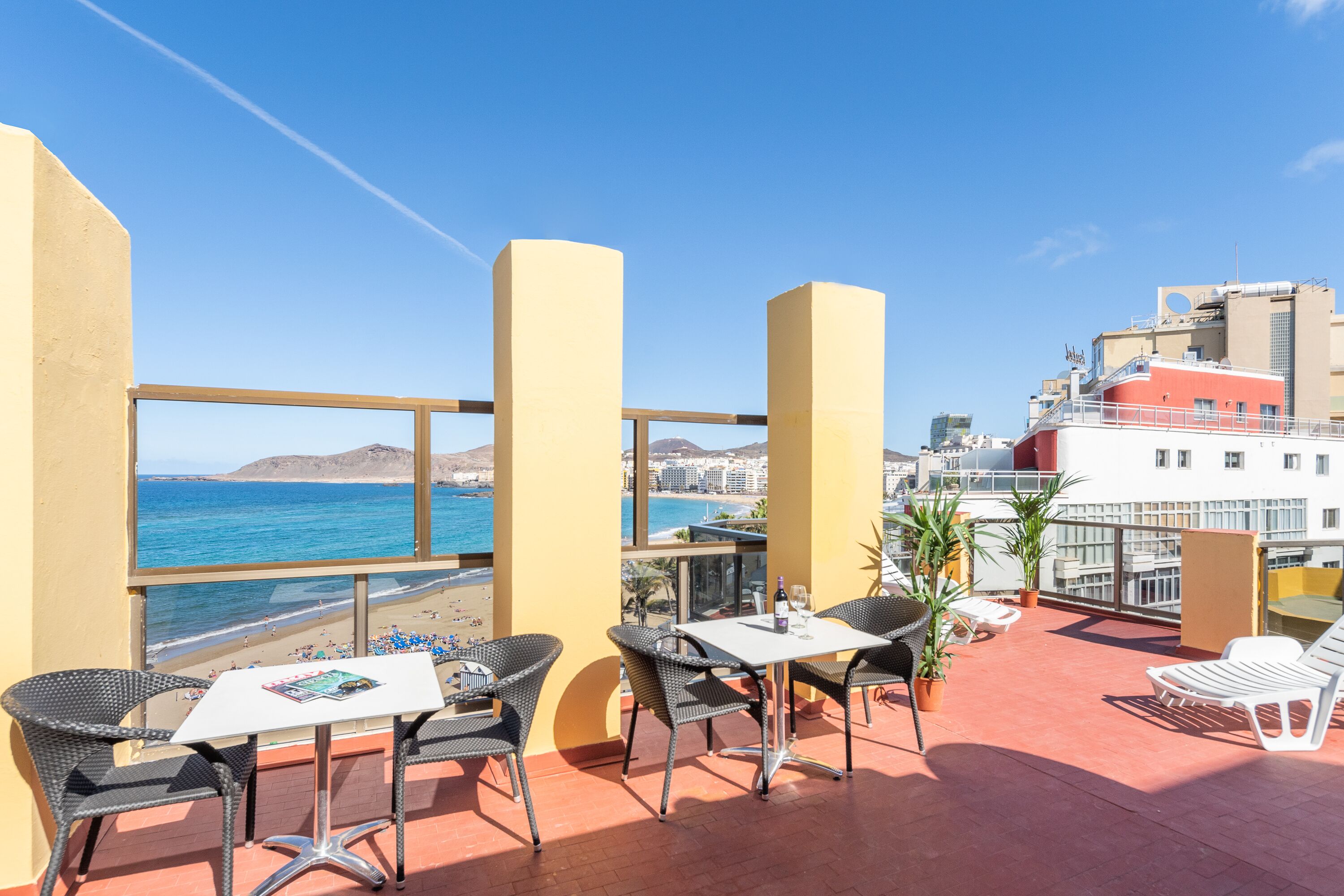 Eine Terrasse mit Tisch und Stühlen mit Blick auf Strand und Stadtlandschaft.
