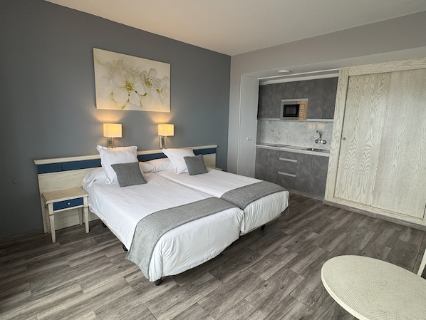Une chambre d’hôtel avec un lit double, des tables de chevet, un petit bureau, une chaise, une kitchenette et une armoire.