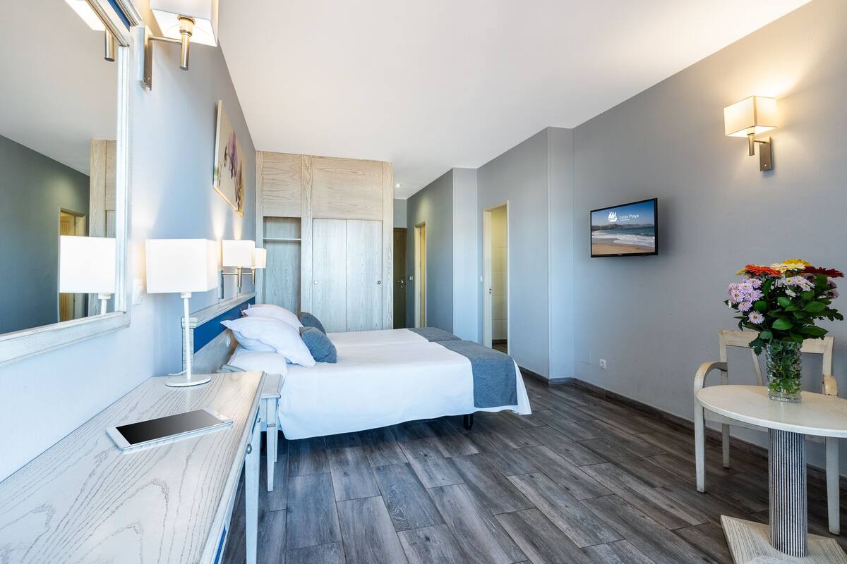 Ein modernes Hotelzimmer mit Bett, Nachttisch, Lampe und einem kleinen Tisch mit Blumenvase.