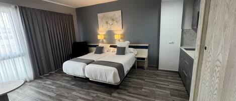 A hotel room with a double bed, bedside tables with lamps, a small desk, a chair, and a large window with curtains.