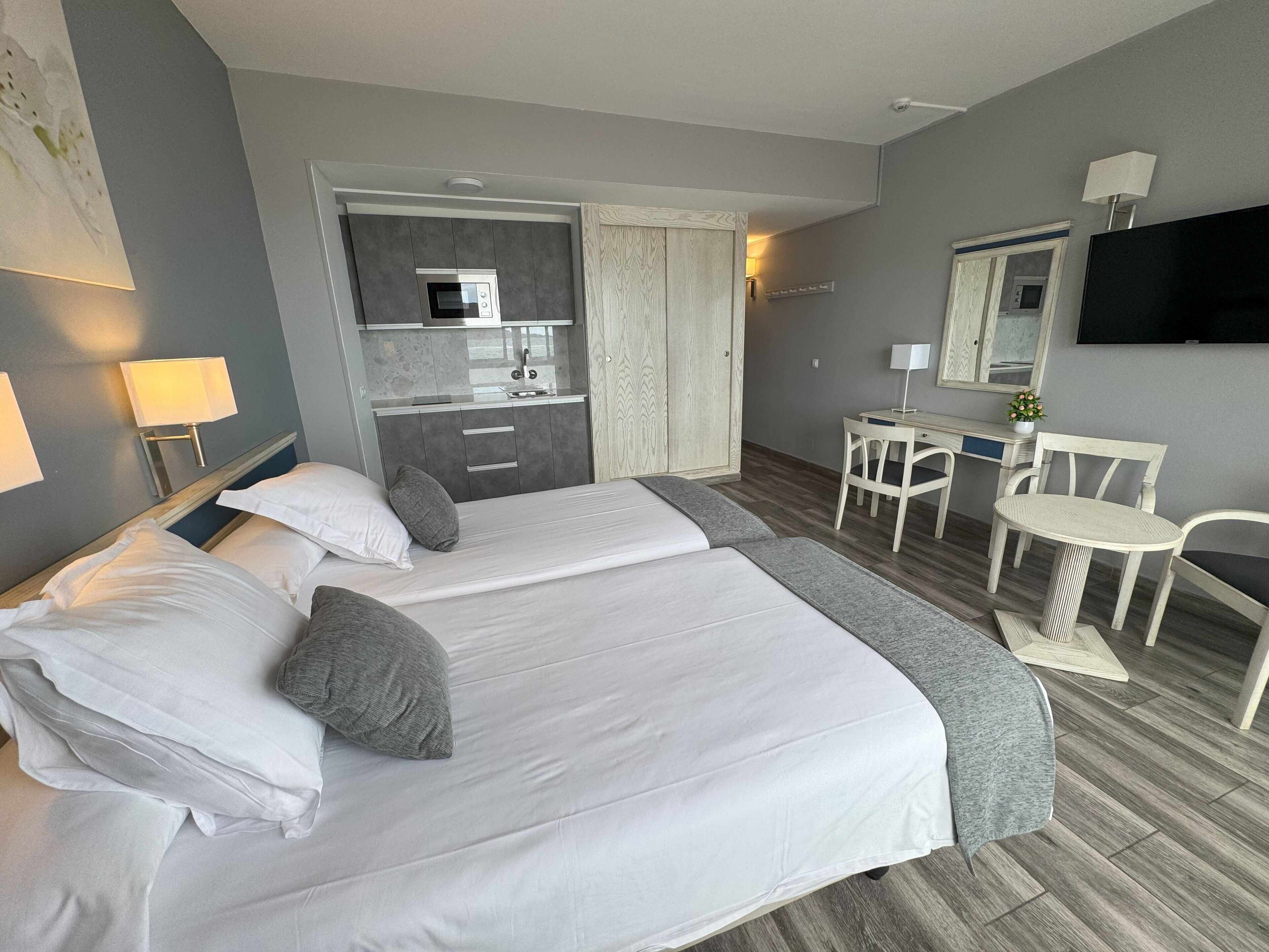 Hotellihuone, jossa on sänky, työpöytä, tuoli, televisio ja pieni keittiönurkkaus.