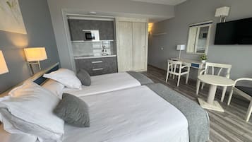 Una habitación de hotel con cama, escritorio, silla, televisor y kitchenette.