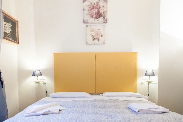 A double bed with a wooden headboard, two bedside lamps, and neatly folded towels.