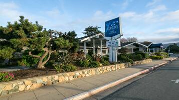 Un hotel llamado Monterey Bay Lodge con un muro de piedra de contención, un jardín ajardinado y un cielo despejado.