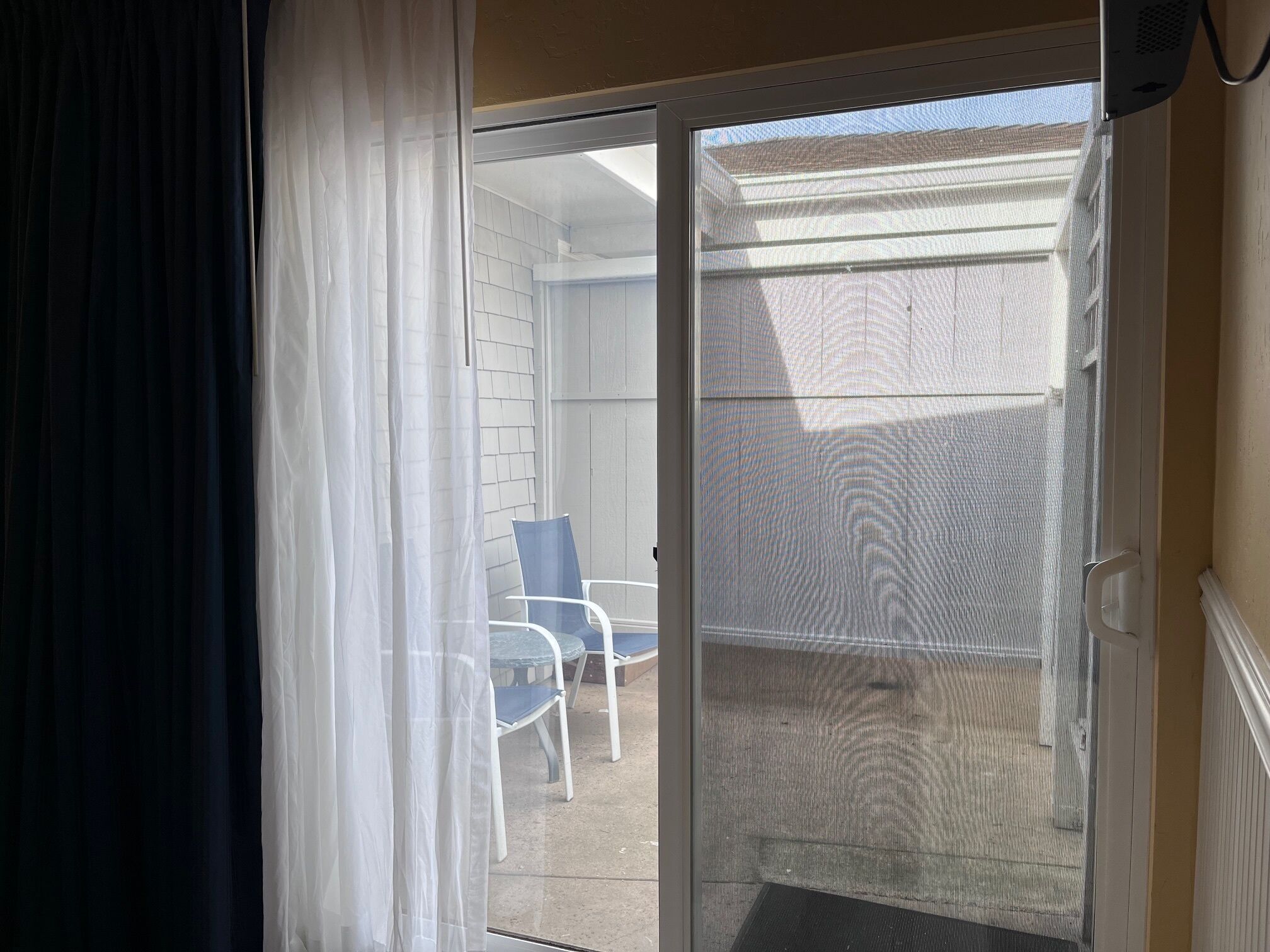 Ein Zimmer mit einer Schiebeglastür, die zu einem Außenbereich mit Terrassenstuhl und weißer Wand führt.