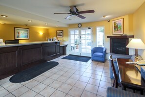 A hotel lobby with a reception desk, a fireplace, a dining area, and a blue armchair.
