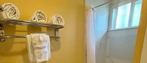A bathroom with a toilet, a shower with a glass door, and a towel rack with towels.
