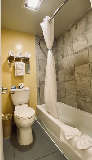 A bathroom with a toilet, a bathtub with a shower curtain, and a towel rack with folded towels.