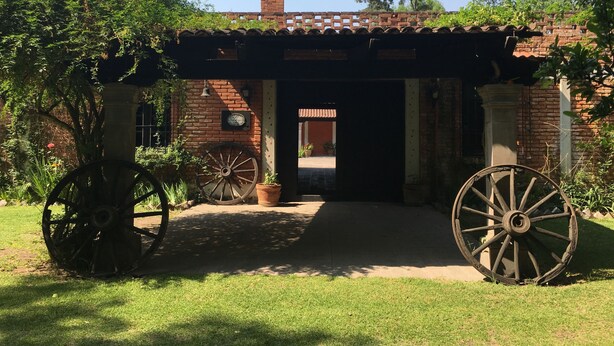 Un edificio rustico con facciata in mattoni, tetto in tegole e una grande ruota di legno in primo piano.