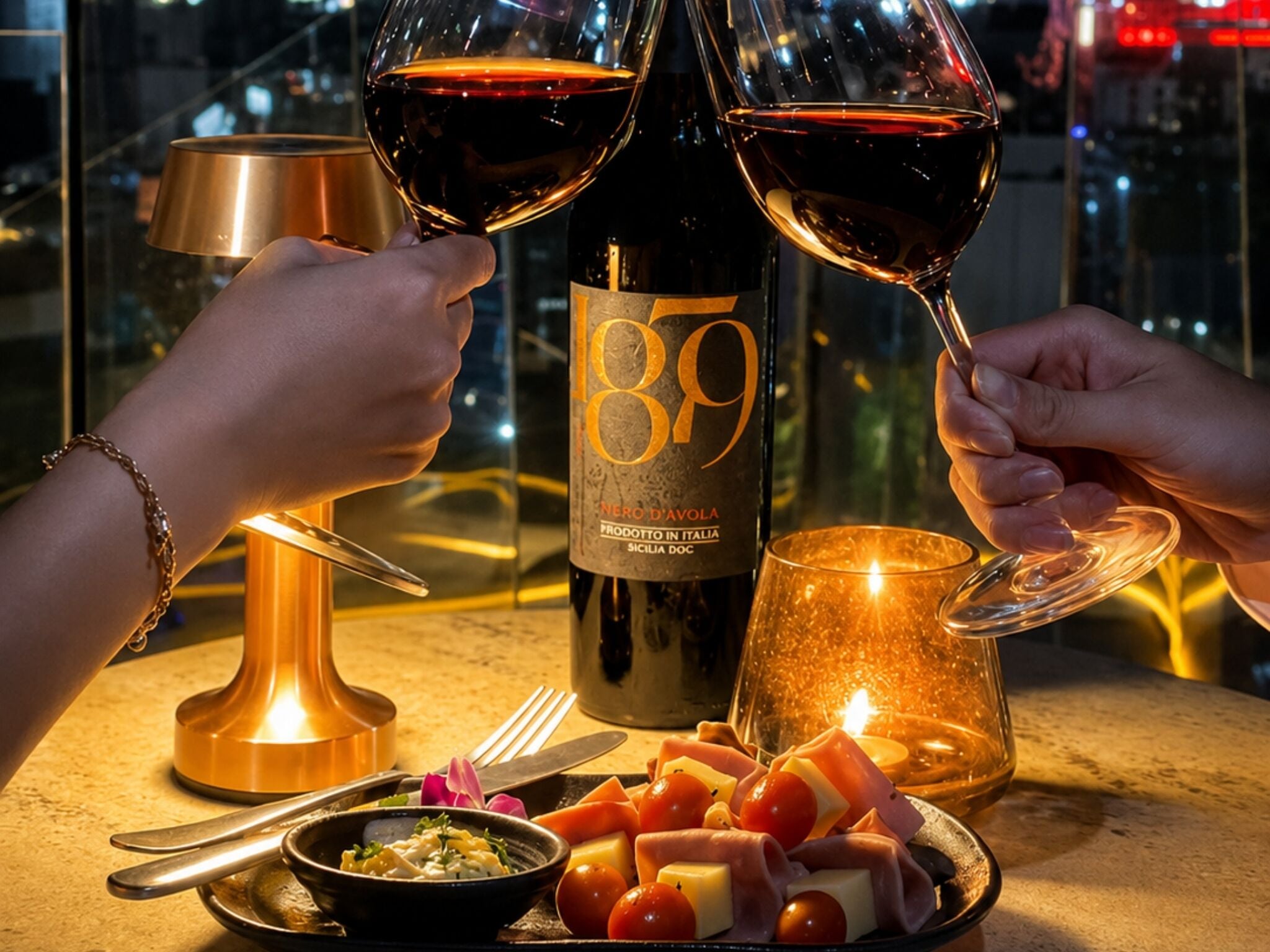 Une table avec une bouteille de vin, deux verres de vin rouge, une bougie et une assiette de fromage et de tomates.